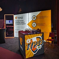Image of a TYPO3 branded event booth with a cube in the forefront, back wall in the back.